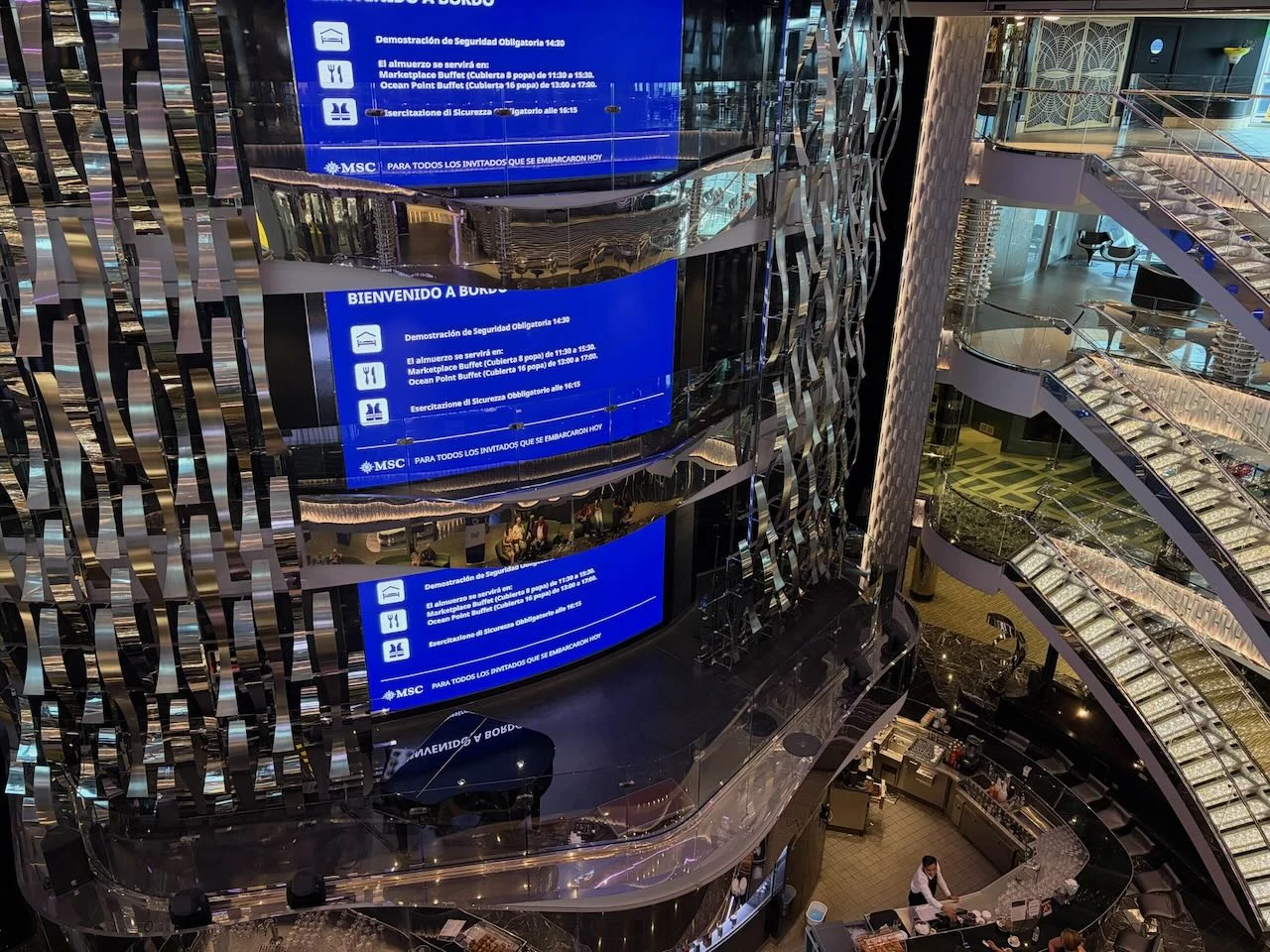 Mehrstöckiges Atrium der MSC Seaview mit großen blauen Informationsbildschirmen und beleuchteten Treppen